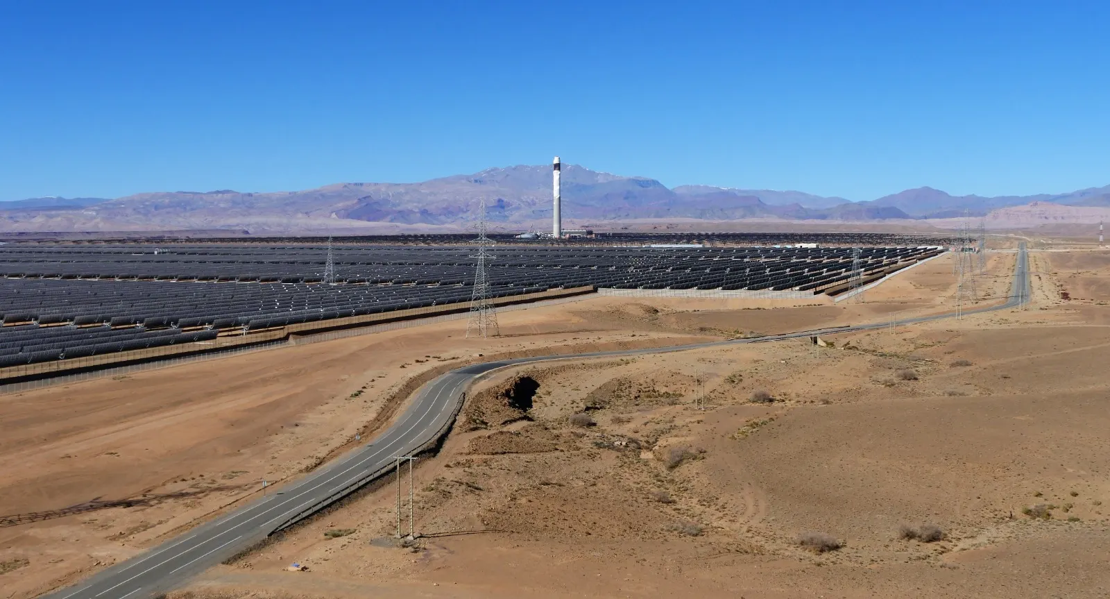 Vaste champ de miroirs solaires et tour centrale dans un paysage désertique, au pied de montagnes